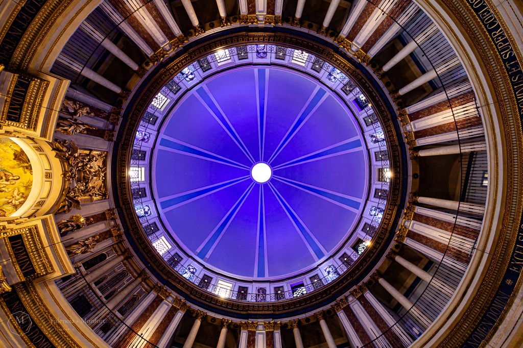 Cúpula con vidriera azul y nervios dorados vista desde abajo, en un interior barroco